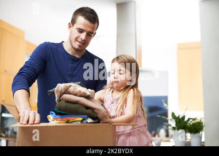 Daddys kleiner Helfer. Ein Vater und eine Tochter packen Kleidung in eine Spendenbox. Stockfoto