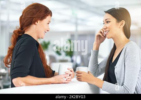 Es ist wichtig, am Arbeitsplatz auszukommen. Zwei Geschäftsfrauen, die ein freundliches Gespräch im Büro führen. Stockfoto