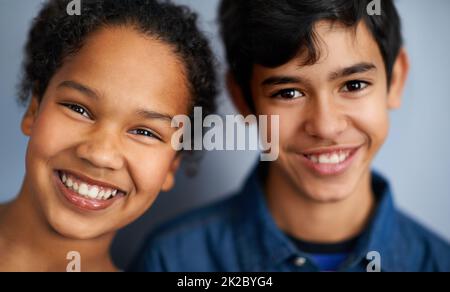 Sie sind Geschwister und beste Freunde. Ein süßer Bruder und eine Schwester stehen isoliert auf grau. Stockfoto