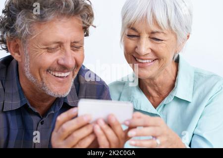 So viele gute zur Auswahl. Ein glückliches Seniorenpaar, das zusammen auf einen Handybildschirm schaut. Stockfoto