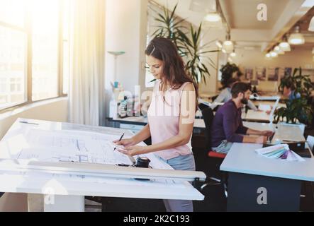 Arbeiten an einem neuen Bauplan. Ausgeschnittene Aufnahme einer jungen Architektin, die an ihrem Entwurfstisch arbeitet. Stockfoto