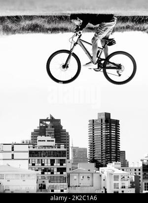 Der Himmel ist die Grenze. Ein Mann auf einem Fahrrad schwebt in der Luft über den Dächern einer Stadt - Wahrnehmung. Stockfoto