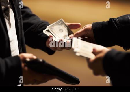 Abschluss des Geschäfts. Hände, die Bargeld halten, und eine Waffe, die Geld zwischen ihnen weitergibt. Stockfoto