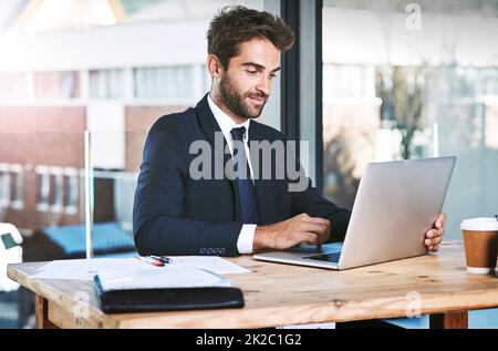 Die Arbeit erledigen. Eine kleine Aufnahme eines hübschen jungen Geschäftsmanns, der im Büro an seinem Laptop arbeitet. Stockfoto