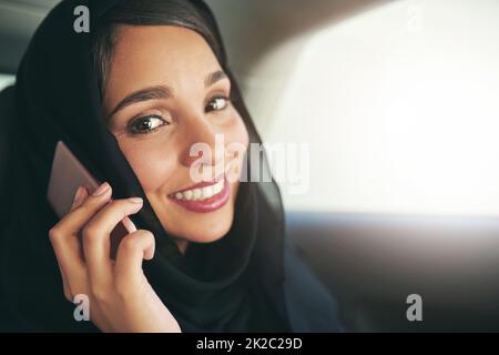 Führungskräfte verlangen Führungsreisen. Aufnahme einer jungen muslimischen Geschäftsfrau, die ihr Telefon benutzte, während sie in einem Auto unterwegs war. Stockfoto