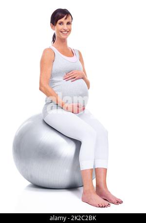 In Form bleiben, bis zu ihrem letzten Trimester. Eine Schwangere lächelt mit einem Pilates Ball, während sie auf Weiß isoliert ist. Stockfoto
