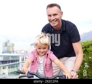 Besondere Momente. Ein hübscher Vater bringt seinem kleinen Sohn das Fahrradfahren bei. Stockfoto