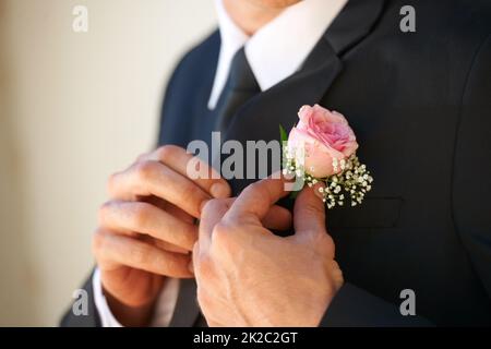 Dafür sorgen, dass er perfekt für seine zukünftige Frau aussieht. Zugeschnittenes Bild eines Bräutigams, der seine Boutonniere vor der Hochzeitszeremonie anpasst. Stockfoto