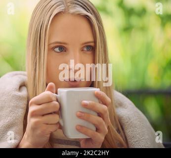 Der einzige Weg mich aufzuwecken. Aufnahme einer jungen Frau, die draußen eine Tasse Kaffee trinkt. Stockfoto