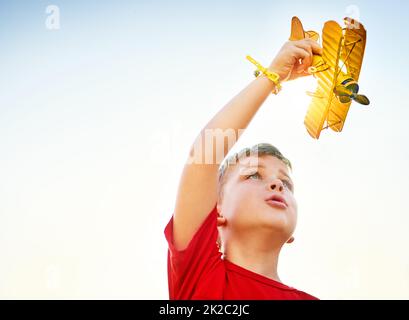 Hoch oben am Himmel. Aufnahme eines kleinen Jungen, der draußen mit einem Spielzeugflugzeug spielt. Stockfoto