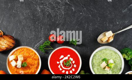 Gesunde Gemüsesuppe mit drei Schalen und Platz zum Kopieren auf dem schwarzen Tisch. Karotten, Tomaten und Broccoli cremig. Konzept der gesunden Ernährung Stockfoto