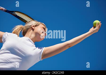 Ihre Gegnerin zu erreichen. Ein junger Tennisspieler, der während eines Spiels dient. Stockfoto