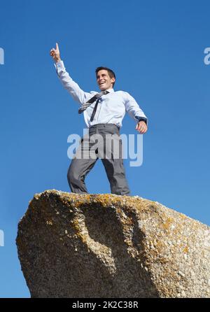 In seiner Karriere aufzusteigen. Ein junger Geschäftsmann, der mit den zum Sieg erhobenen Armen auf einer Klippe steht. Stockfoto