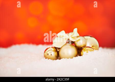 Wir werden festlich. Studioaufnahme eines Arrangements von goldenen Weihnachtsdekorationen vor rotem Hintergrund. Stockfoto