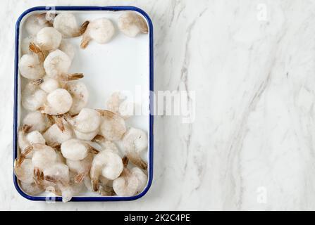 Gefrorene, geschälte gekochte Garnelen in der Kochplatte auf dem weißen Marmortisch, Ansicht von oben, flach liegend, mit Platz für Text Stockfoto