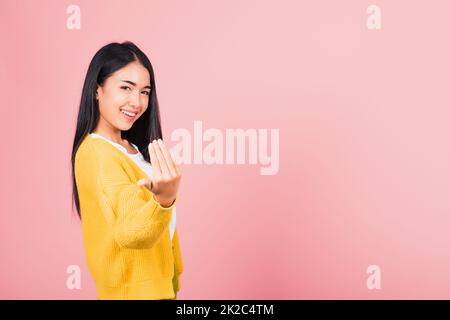 Fröhliches asiatisches Porträt schöne süße junge Frau Teenager positiv freundlich Geste Hand einladend hierher zu kommen mit Hand Look to Camera Studio aufgenommen isoliert auf pinkfarbenem Hintergrund mit Kopierbereich Stockfoto