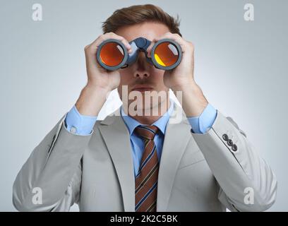 Spionage gegen die Konkurrenz. Ein junger Geschäftsmann schaut durch ein Fernglas. Stockfoto
