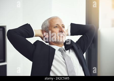 Sich um das Geschäft kümmern. Aufnahme eines selbstbewussten, reifen Geschäftsmannes, der sich in einem Büro mit den Händen hinter dem Kopf auf dem stuhl von hais zurücklehnt. Stockfoto