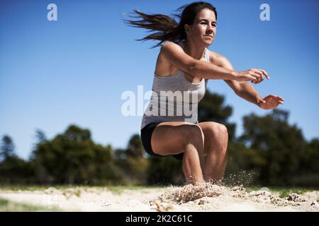 Geht so weit wie möglich. Eine junge Frau, die Weitsprung macht. Stockfoto