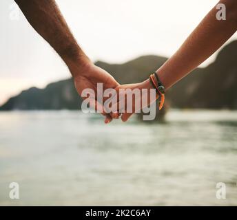 Erkunde die Welt mit der, die du liebst. Nahaufnahme eines jungen Paares, das die Hände am Strand hält. Stockfoto