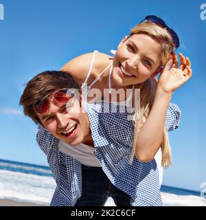 Der beste Sommer aller Zeiten. Aufnahme eines glücklichen jungen Paares, das eine Huckepack-Fahrt am Strand genießt. Stockfoto