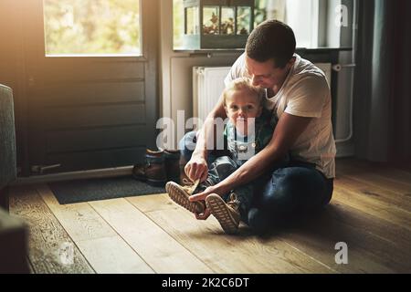 Machen Sie sich bereit für einen Tag. Aufnahme eines Vaters, der seinem Sohn hilft, sich zu Hause die Schuhe anzuziehen. Stockfoto