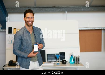 Stolz darauf, meine neue App für android-Handys zu starten. Porträt eines jungen Mannes, der den Bildschirm eines Mobiltelefons in einem modernen Büro zeigt. Stockfoto