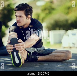 Sein Aufwärmen ist der Schlüssel zu seinem Workout. Ganzkörperaufnahme eines hübschen jungen Mannes, der sich vor dem Training im Freien aufwärmt. Stockfoto