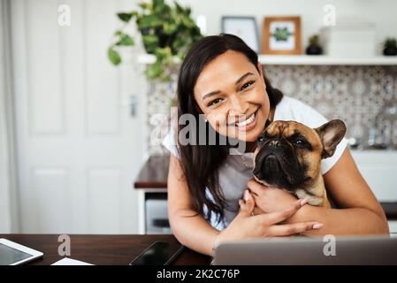 Der Weg zu meinem Herzen ist voller Pfotenabdrücke. Porträt einer jungen Frau, die mit ihrem Hund auf dem Schoß sitzt, während sie von zu Hause aus arbeitet. Stockfoto