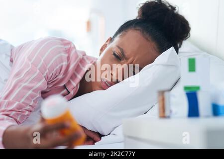 Ich Frage mich, ob diese Pillen mir helfen, mich besser zu fühlen. Aufnahme einer attraktiven jungen Frau, die zu Hause eine Flasche Pillen im Bett hält. Stockfoto