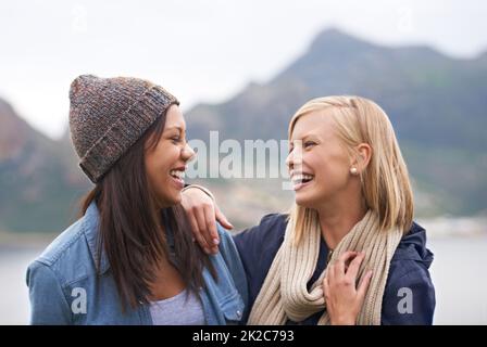 Den Tag mit Freundschaft und Lachen aufwärmen. Zwei glückliche junge Frauen lächeln am Strand. Stockfoto