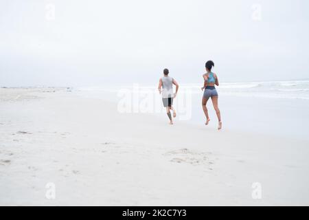 Ihre Strandkörpern für den Sommer vorbereiten. Rückansicht eines jungen Paares, das zusammen am Strand entlang läuft. Stockfoto