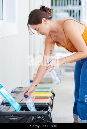 Umweltbewusst zu sein ist mir wichtig. Aufnahme einer attraktiven jungen Frau, die sich hinstellt und Plastikflaschen in ihren Papierkorb legt. Stockfoto