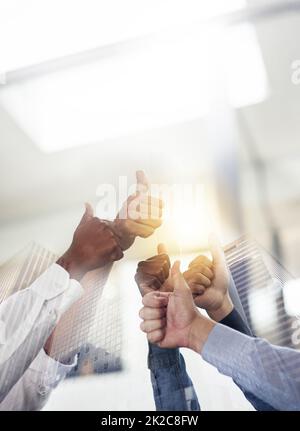 Teamwork ist ein tolles Gefühl. Aufnahme von Wolkenkratzern, die über einem nicht identifizierbaren Geschäftsteam mit Daumen nach oben übereinander gelegt wurden. Stockfoto