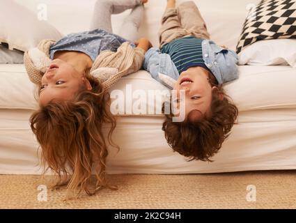 Herumhängen, ohne etwas zu tun. Aufnahme von zwei kleinen Kindern, die auf einem Sofa liegen und ihre Köpfe über dem Rand hängen. Stockfoto