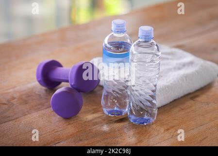 Alles, was ich für mein Training brauche. Ein Schuss Hanteln, Wasserflaschen und ein Handtuch auf einem Holztisch. Stockfoto