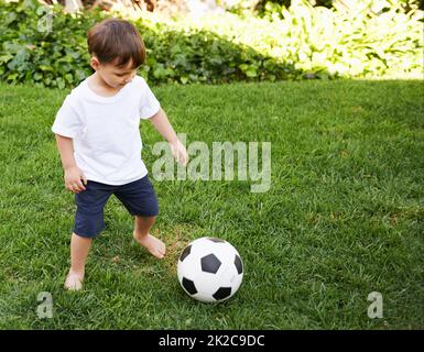 Fußball im Hinterhof. Ein süßer kleiner Junge mit einem Fußball im Hinterhof. Stockfoto