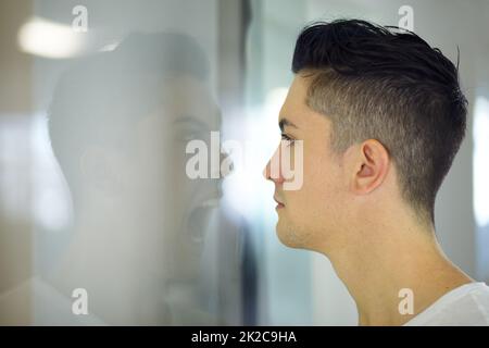 Schreiend drinnen. Junger Mann, der auf eine schreiende Spiegelung seiner selbst schaut. Stockfoto