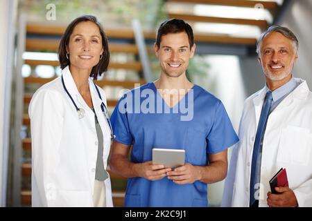 Waren hier, um zu helfen. Ein zugeschnittenes Porträt eines hübschen jungen Arztes, der mit einer Tablette zwischen zwei seiner Kollegen steht. Stockfoto