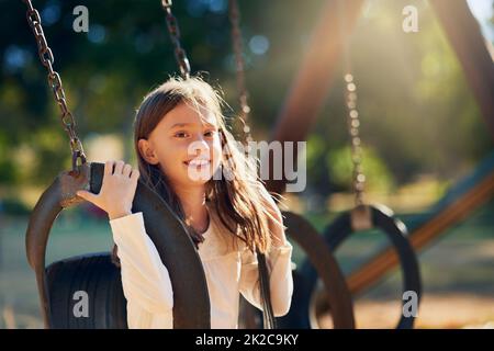 Schwingt in einen tollen Tag. Aufnahme eines glücklichen kleinen Mädchens, das sich auf den Schaukeln auf dem Spielplatz amüsieren kann. Stockfoto