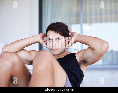 Seine Fitnessziele sind immer in Sicht. Eine kurze Aufnahme eines fokussierten jungen Mannes, der zu Hause Sit-ups macht. Stockfoto