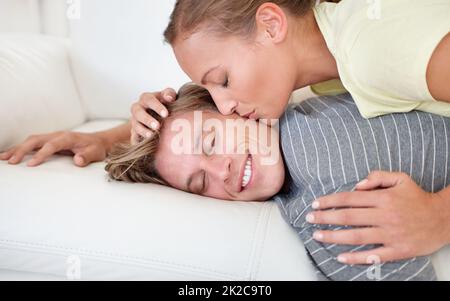 Was für eine angenehme Art aufzuwachen. Aufnahme einer Frau, die sich überlehnt und ihren Freund auf einem Sofa liegend küsst. Stockfoto