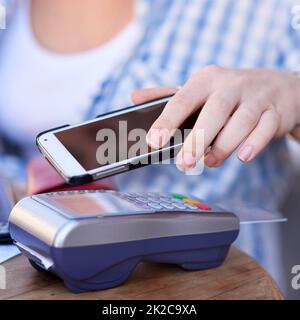 Technologie macht es heutzutage so einfach, zu zahlen. Foto einer nicht identifizierbaren Frau, die eine mobile Zahlung mit ihrem Smartphone und einem Kartenautomaten in einem Café tätigt. Stockfoto