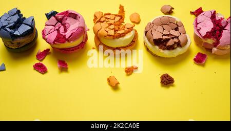 Gebrochene runde Makronen mit Krümel auf gelbem Hintergrund, leckeres Dessert, Draufsicht Stockfoto