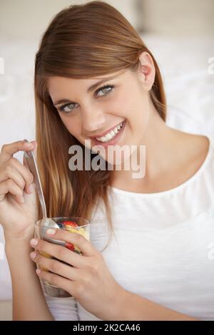 Genießen Sie ihre neue Ernährung. Eine attraktive junge Frau, die einen Obstsalat isst. Stockfoto