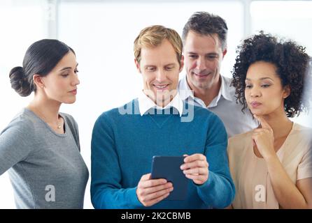 Gemeinsam erreichen alle mehr. Eine Gruppe von Kollegen nutzt gemeinsam ein digitales Tablet. Stockfoto