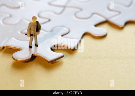 Eine kleine Arbeiterfigur am Rand verknüpfter Puzzleteile. Nahaufnahme von Puzzleteilen, die auf gelbem Papier miteinander verbunden sind Stockfoto