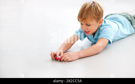 Vroom Vroom Aufnahme eines entzückenden kleinen Jungen, der mit einem Spielzeugauto spielt. Stockfoto