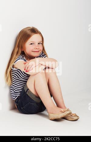 Zu niedlich für Worte. Studioportrait eines entzückenden kleinen Mädchens, das mit dem Rücken gegen die Wand sitzt. Stockfoto