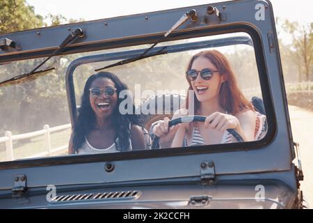 Spaß ist unser Treibstoff. Kurzer Schuss von zwei lachenden Frauen, die auf einer unbefestigten Straße fahren. Stockfoto